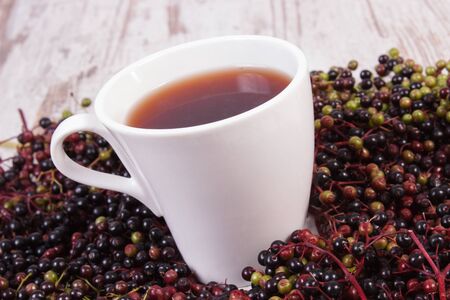 Cup of hot tea with elderberry juice and heap of berry in background, healthy nutrition, alternative medicine and therapyの写真素材