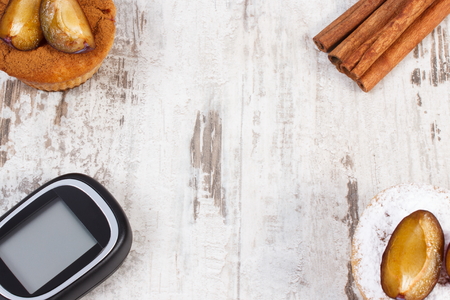 Glucose meter, muffins with plums and cinnamon sticks on old rustic wooden background, copy space for text, diabetes and delicious dessertの写真素材