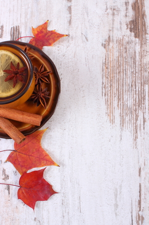 Cup of hot tea with lemon, spices and autumnal leaves on old rustic wooden background, autumn concept, copy space for textの写真素材