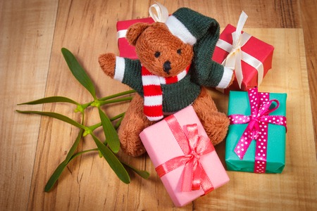 Fluffy teddy bear with wrapped colorful gifts for Christmas or other celebration and green mistletoe...