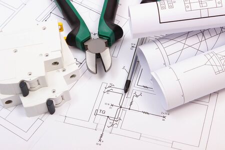 Metal pliers, screwdriver, electric fuse and rolls of diagrams on electrical construction drawing of...