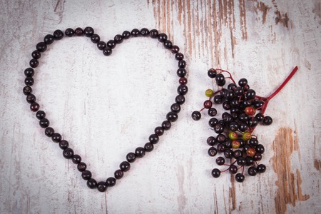 Heart shaped fresh elderberry and bunch of fresh berry on old rustic wooden background, symbol of...
