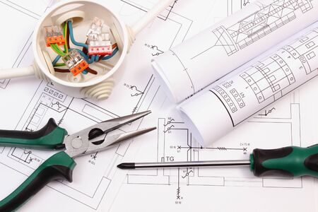 Work tools, rolls of diagrams and cable connections in electrical box lying on construction drawing,...
