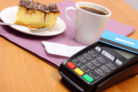Use payment terminal and credit card for paying in cafe or restaurant, cheesecake and coffee, enter personal identification number, polish receipt, finance conceptの写真素材
