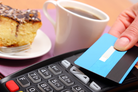 Use payment terminal with contactless credit card with NFC technology for paying in cafe or restaurant, cheesecake and coffee, finance conceptの写真素材