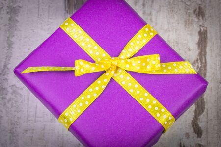 Wrapped in purple paper gift for Christmas, birthday or other celebration on old wooden white plank
