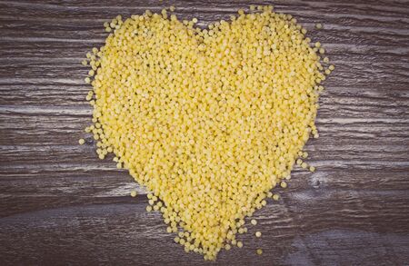 Heart shaped yellow millet groats on wooden background, concept for healthy eating and nutrition, symbol of loveの写真素材