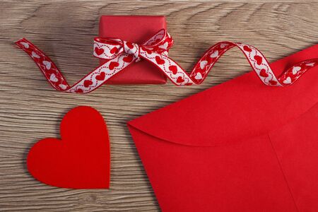 Wrapped gift with ribbon, red wooden heart and love letter in envelope on wooden background,...