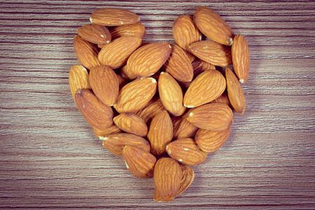 Vintage photo, Heart shaped fresh healthy almonds on wooden background, concept for healthy nutrition, symbol of loveの写真素材