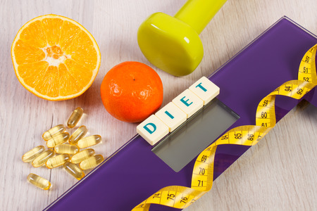 Tape measure on household digital bathroom scale for weight of human body, dumbbells for fitness, fresh fruits and tablets supplements, concept of healthy lifestyle and slimmingの写真素材