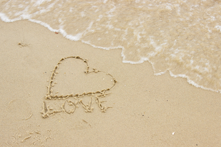 Word love and shape of heart written on sand at the beach by the sea, symbol of love, summer timeの写真素材