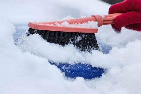 Hand of woman using brush and remove snow and ice from car and windscreen, concept of transportation and winterの写真素材