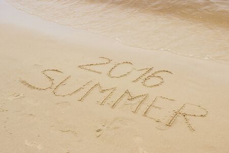Summer 2016 written on sand at the beach by the sea, summer and vacation timeの写真素材