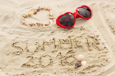 Summer 2016 written on sand at the beach and heart of shells with sunglasses, summer time, symbol of loveの写真素材