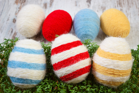 Easter eggs wrapped woolen string and green cuckooflower cress on old wooden background, decoration for Easterの写真素材