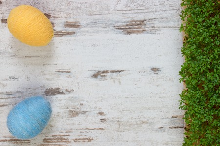 Easter eggs wrapped woolen string and green cuckooflower cress on old wooden background, copy space...