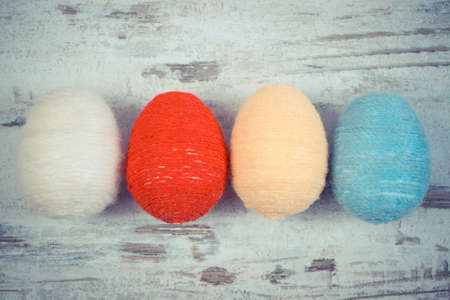 Vintage photo, Easter eggs wrapped woolen string on old rustic wooden background, decoration for Easterの写真素材