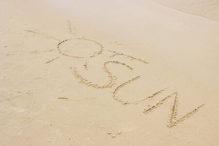 Word sun and shape of sun written on sand at the beach by the sea, summer and vacation timeの写真素材