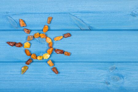Amber stones in shape of sun on blue boards, copy space for text or inscription, summer and vacation timeの写真素材