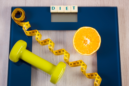 Tape measure, fresh orange and green dumbbells for fitness on digital bathroom scale for weight of human body, concept of healthy lifestyle and slimmingの写真素材