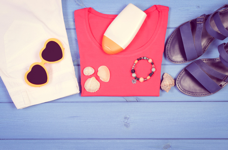 Vintage photo, Clothing for woman and accessories for vacation and summer on purple boards, sunglasses, sun lotion, leather sandals, shirt, pantsの写真素材