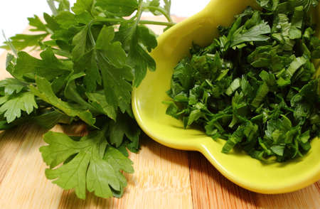 Bunch of fresh natural and green parsley and chopped parsley in background lying on wooden cutting board, concept for healthy eatingの写真素材