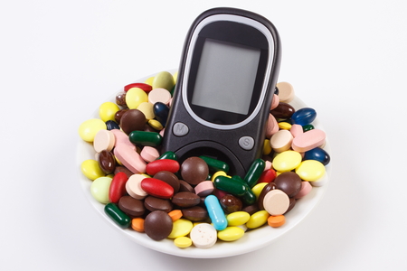 Glucose meter and heap of colorful medical pills, capsules or supplements for therapy, concept of treatment, diabetes and health careの写真素材