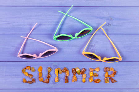 Inscription summer made of amber stones and sunglasses on purple boardsの写真素材