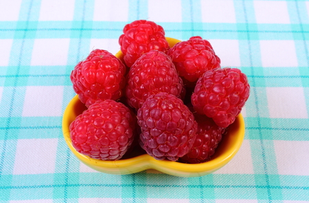 Fresh raspberries in yellow bowl on checkered tablecloth