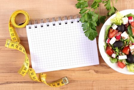 Fresh greek salad with vegetables, tape measure and notepad for writing notesの写真素材