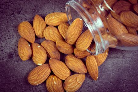 Vintage photo, Heap of fresh healthy almonds spilling out of glass jar on structure of concreteの写真素材
