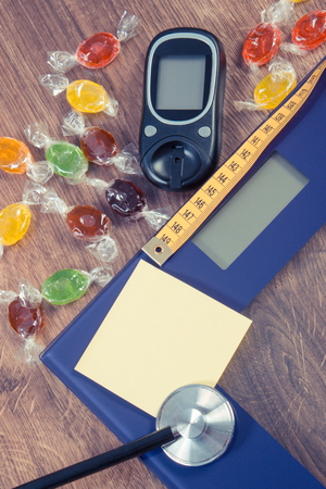 Electronic bathroom scale, glucose meter, stethoscope, tape measure and heap of colorful candies, diabetes, slimming and reduction eating sweets, copy space for text on sheet of paperの写真素材