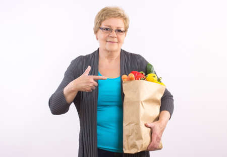Happy smiling elderly senior woman showing shopping bag with fruits and vegetablesの写真素材