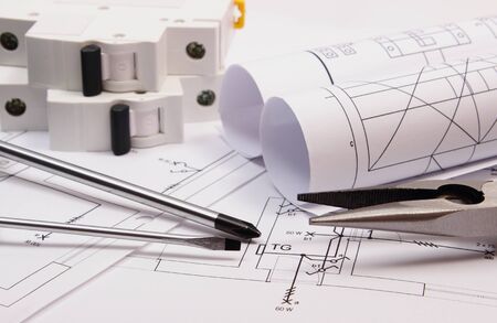 Metal pliers, screwdriver, electric fuse and rolls of diagrams on electrical construction drawing,...