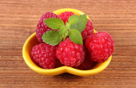 Fresh raspberries and leaf of lemon balm in yellow bowl on wooden table, concept of healthy food and...