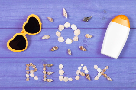 Inscription relax and shape of sun made of seashells, sunglasses and sun lotion on purple boards,...