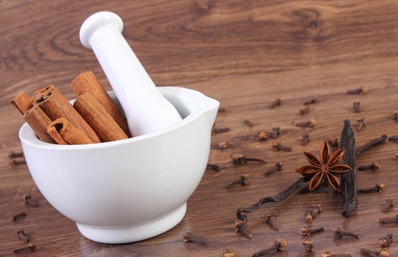Fresh fragrant cinnamon sticks in white glass mortar and spices on rustic wooden boardの写真素材