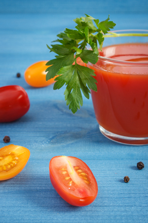 Glass of fresh tomato juice and vegetables with spices on blue board, healthy nutritionの写真素材