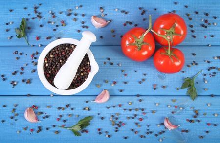 Colorful pepper in white glass mortar and fresh vegetables on blue boards, seasoning for cookingの写真素材