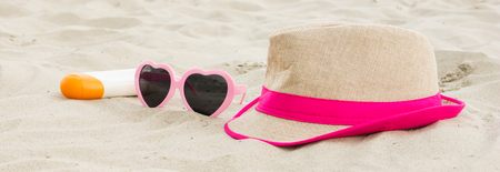 Sunglasses, straw hat and bottle of sun lotion on sand at beach, sun protection on vacation, summer timeの写真素材