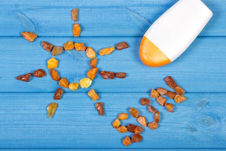 Word and shape of sun made of amber stones, sun lotion on blue boards, summer and vacation time