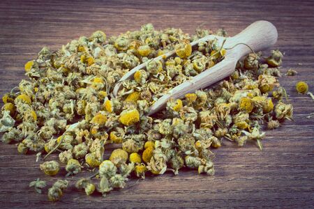 Vintage photo, Heap of dried chamomile with wooden spoon lying on wooden board, concept of healthy nutrition, herbalism and alternative medicineの写真素材