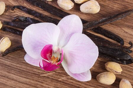 Pistachio nuts, blooming orchid flower and fragrant vanilla sticks pods on wooden background, cosmetics ingredientsの写真素材