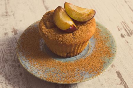 Vintage photo, Homemade fresh baked muffins with plums and powdery cinnamon on plate on old rustic wooden background, delicious dessertの写真素材