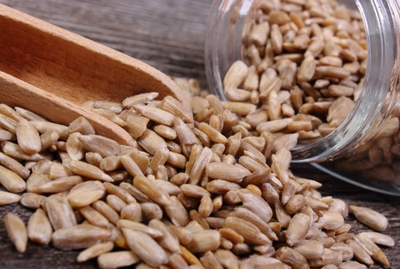 Heap of sunflower seeds spilling out of glass jar on wooden background, concept of healthy eating and nutritionの写真素材