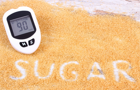 Glucose meter with result of measurement sugar level and natural brown cane sugar, concept of diabetes and reduction eating sweets, copy space for textの写真素材