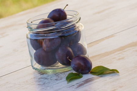 Heap of fresh plums in glass jar on wooden rustic table in garden, healthy nutrition, preparation for preserved plumsの写真素材