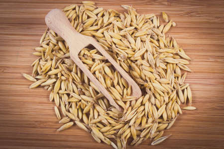 Vintage photo, Heap of organic oat grains on wooden spoon lying on wooden table, healthy food and nutritionの写真素材