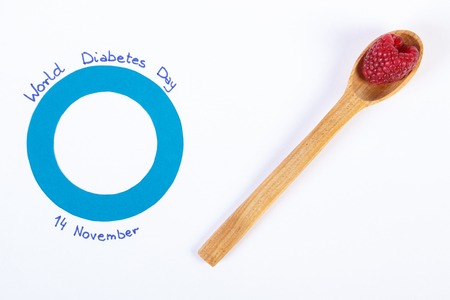 Fresh ripe raspberries and blue circle of paper, symbol of world diabetes day. White background