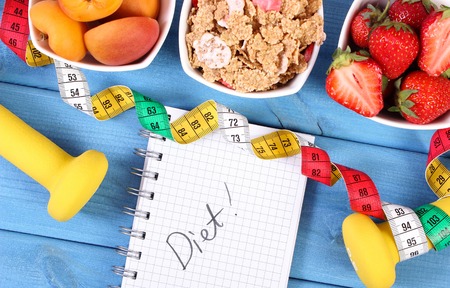 Fresh healthy food, dumbbells for fitness, tape measure and notebook for writing notes on boards, concept of slimming, healthy, sporty lifestyleの写真素材